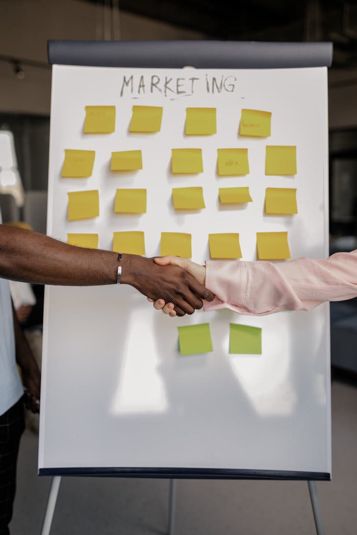 Colleagues shaking hands in front of a marketing board during a business meeting.